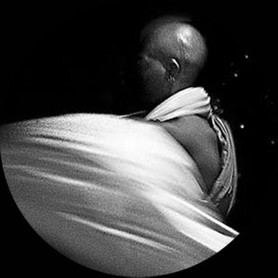 Exu, 2005, da série Heranças compartilhadas. Foto: Denise Camargo
Esta imagem, tomada em preto-e-branco, durante um ritual em templo da religião vodu, em Nova Orleans, Estados Unidos, retrata um homem negro, alto, com a cabeça completamente nua e de perfi, vestindo uma espécie de capa que aparece em cor branca e presa, transversalmente, em um dos ombros. O segundo plano, ao fundo, é escuro. Não podemos ver o seu rosto, pois só a parte lateral de seu corpo está iluminada. Ele está incorporado pela divindade Exu e dança. A imagem registra o seu movimento. Segundo a mitologia, Exu tem um temperamento irascível e brincalhão. É o mensageiro que propicia a comunicação entre homens e os outros deuses de origem africana. E deve ser sempre o primeiro a receber oferendas, por isso é colocado à entrada das casas.